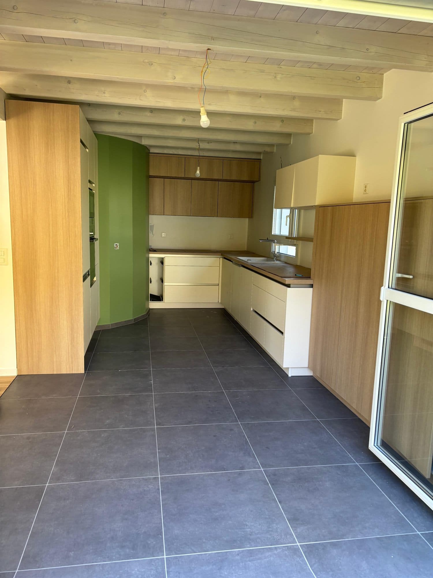 La même cuisine terminée : agencement posé, mur courbe vert et carrelage anthracite