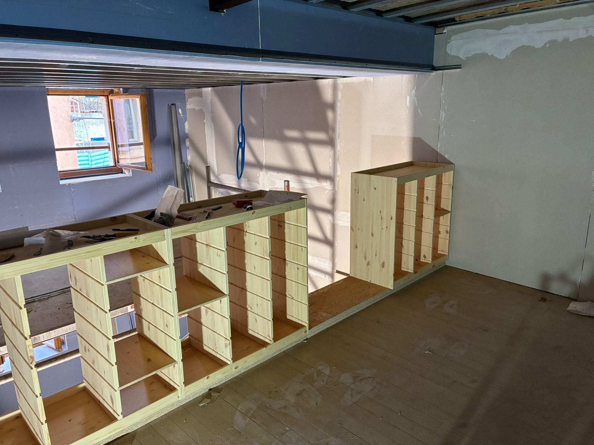 Meuble de rangement en bois brut en cours de montage sur la mezzanine, cloisons non finies