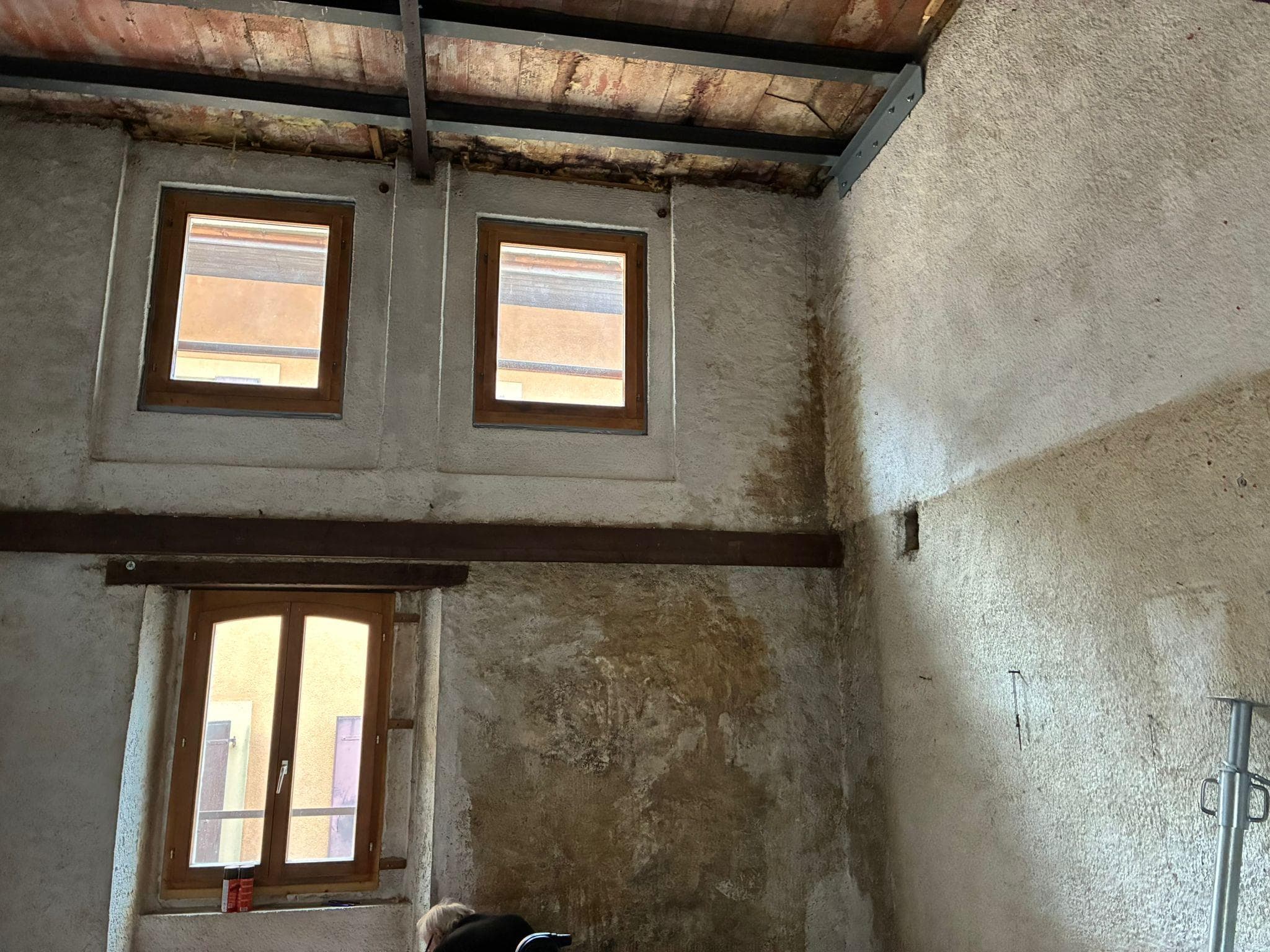 Séjour avant travaux : murs en pierre dégradés, plafond à voûtains et poutre apparente