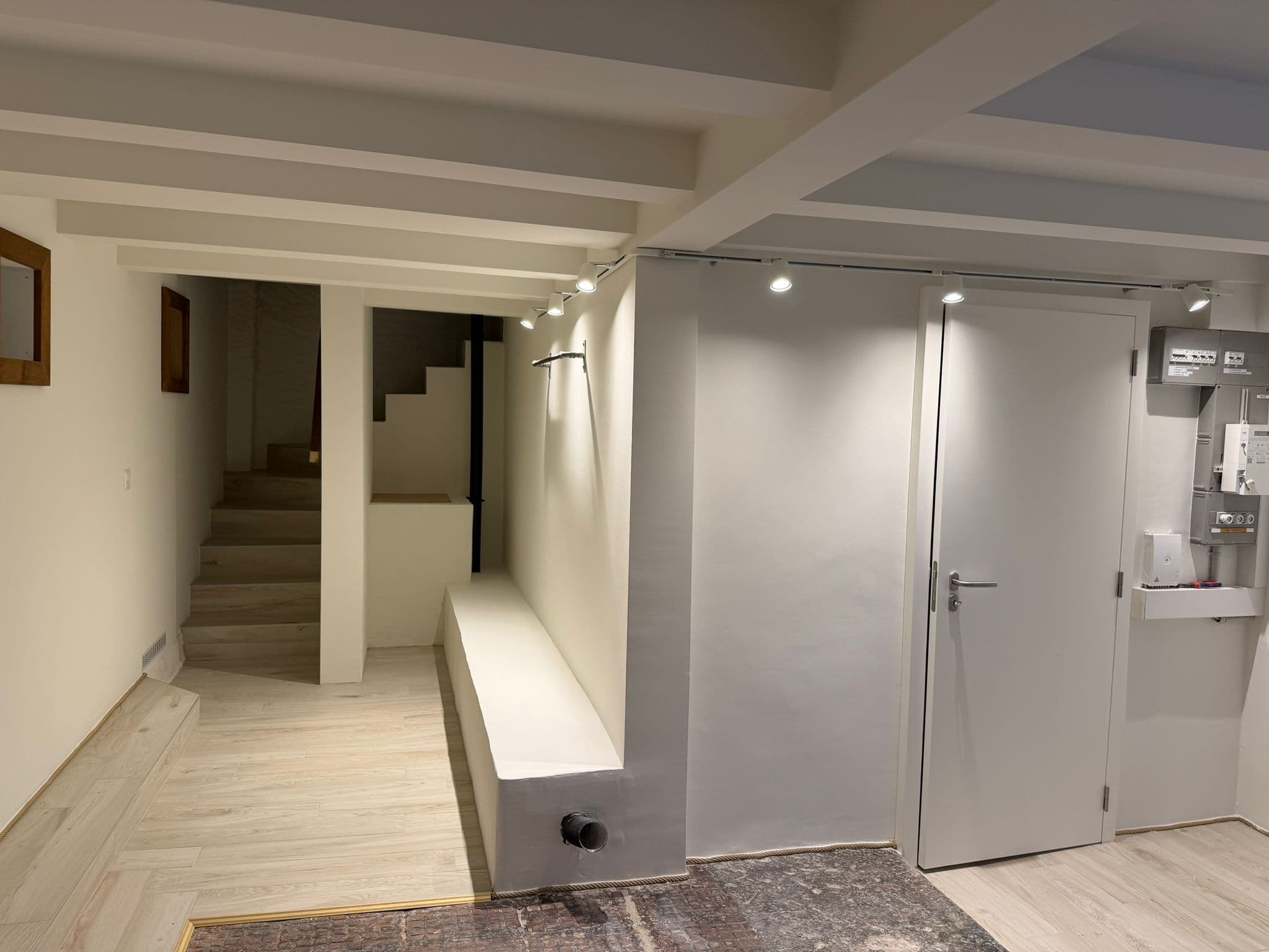 Le même espace transformé en hall d’entrée : plafond et murs peints en blanc, sol carrelé effet bois