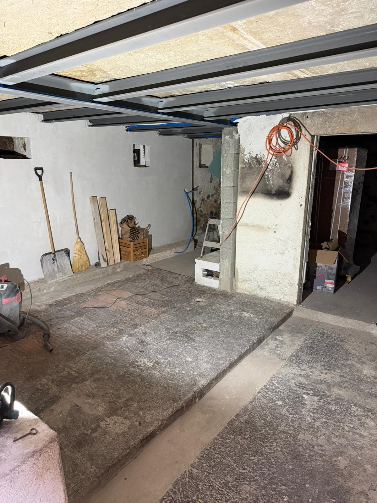 Sous-sol avant aménagement : dalle béton brute, poutrelles métalliques apparentes et matériel de chantier
